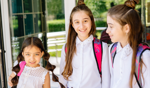 Three female children in school uniform walking through door