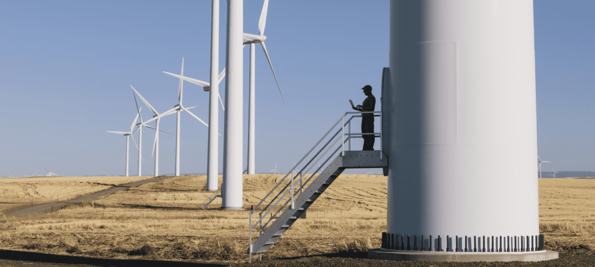 lone engineer standing on the steps of a large wind turbine in the countryside