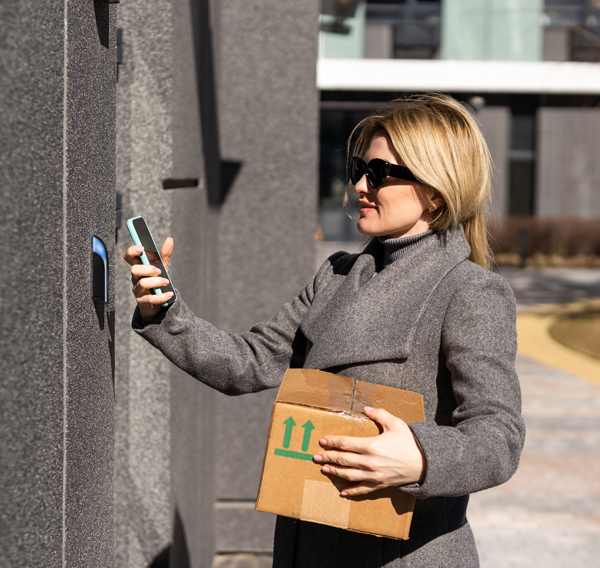 Woman in a coat holding a parcel uses her mobile to access a door